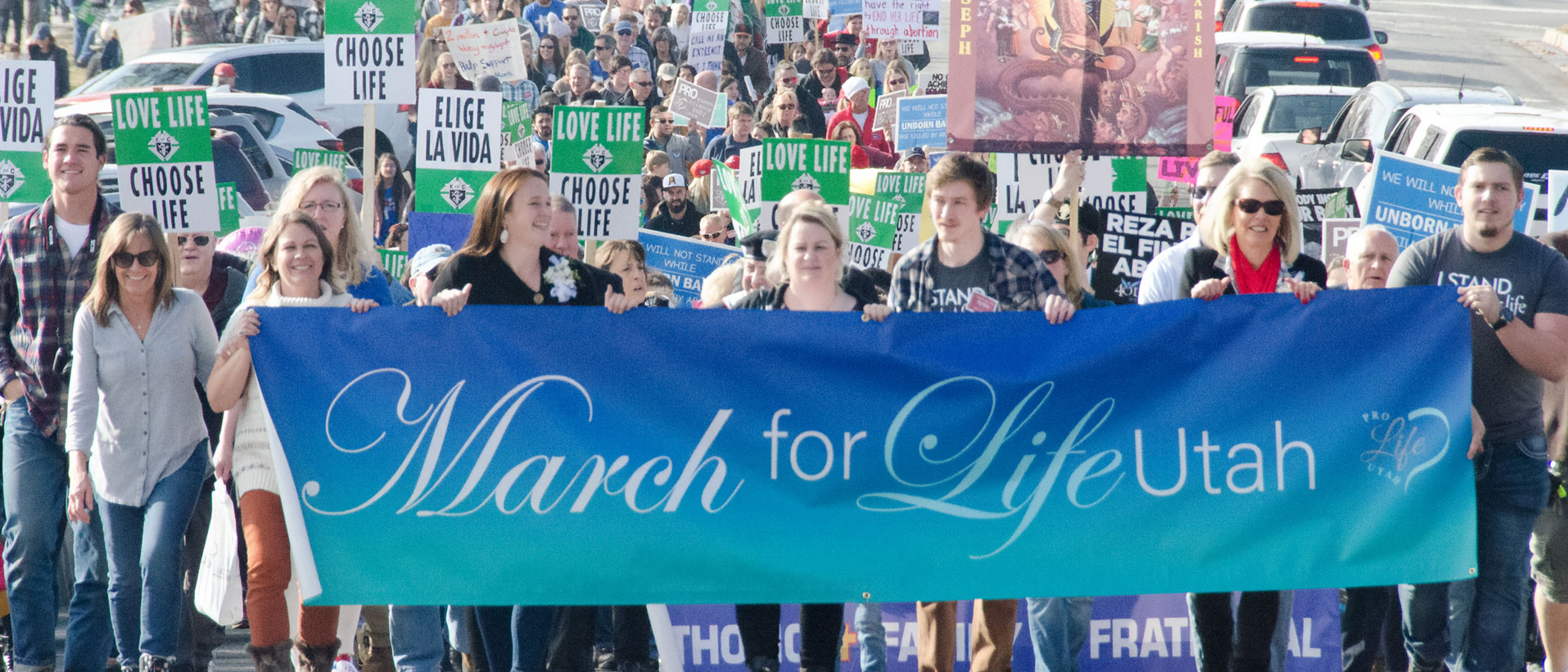 Marchers carrying a March for Life Utah banner down the street, followed by a crowd with Choose Life signs